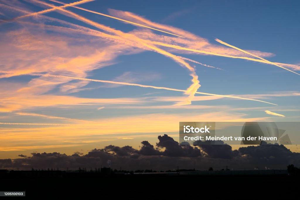 Contrails high up in the sky are colorful illuminated by the light of the setting sun Colorful contrails with nice contrast with the blue sky. Below, closer to the surface of the earth, there are dark clouds. Airplane Stock Photo