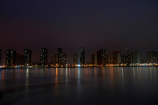 Residential complex of high-rise buildings with lighted windows on the shore of a frozen lake at night