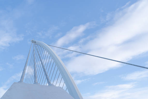 Dublin, Ireland - February 8, 2020: Two pedestrians crossing the River Liffey using the Samuel Beckett Bridge (designed by Santiago Calatrava, constructed in  2009).  In the distance is the city centre skyline.