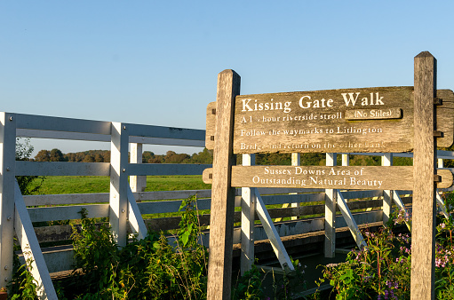 Wooden sign by a bridge under a clear blue sky  in summer in the Wealden district. Also showing directions to Litlington, East Sussex, UK