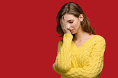 Caucasian young women in yellow jumper at the studio on the red background. She is very sad, annoyed, possibly sick.