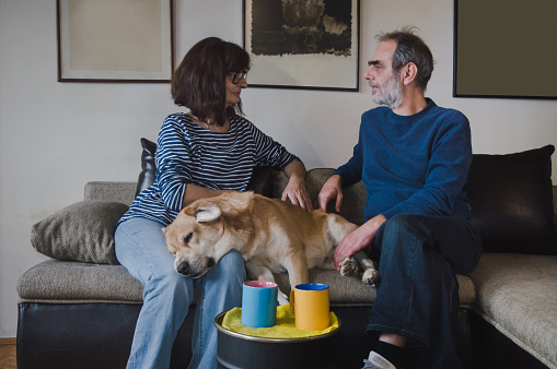 Elder couple sitting on sofa with dog and drinking coffee