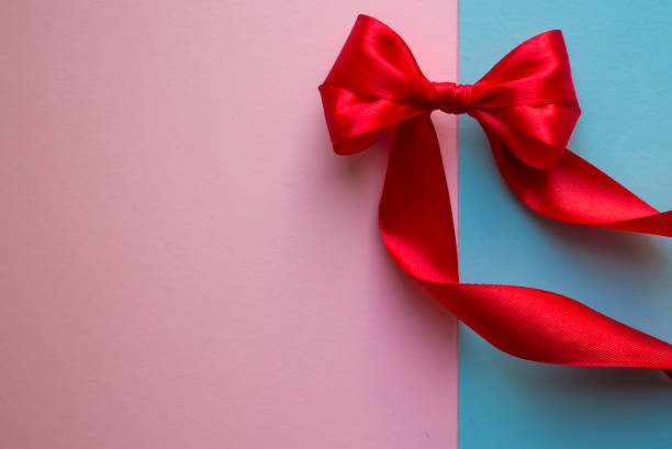 istock Bright red bow made from silk ribbon on blue and pink background. Festive concept with copy space on the left side. Birthday greetings concept. Close up 1205116043