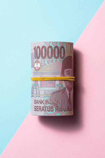 rupia indonesiana rotola su sfondo a due colori - indonesian currency foto e immagini stock