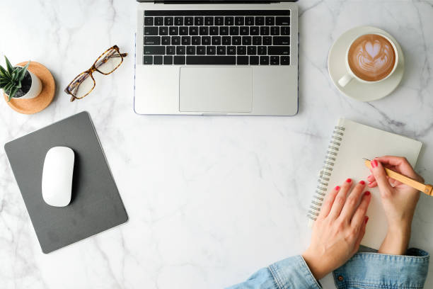 istock Flat lay workspace. Woman hand with coffee cup, smartphone, computer, notebook, planner and stationary with copy space on marble table background. Top view. modern style. 1205131610