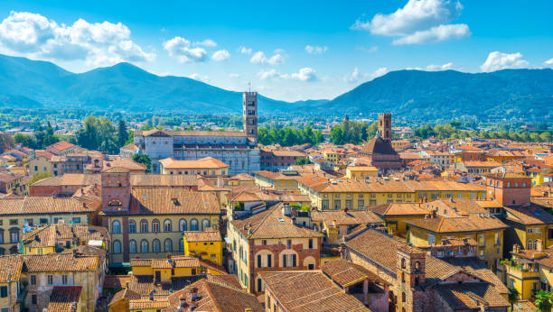 Aerial top panoramic view of historical centre medieval town Lucca with old buildings, typical orange terracotta tiled roofs and mountain range, hills, blue sky white clouds background, Tuscany, Italy Aerial top panoramic view of historical centre medieval town Lucca with old buildings, typical orange terracotta tiled roofs and mountain range, hills, blue sky white clouds background, Tuscany, Italy lucca stock pictures, royalty-free photos & images