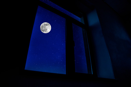 Night scene of moon seen through the window from dark room. Moonlight inside dark room