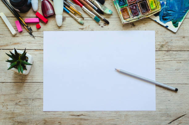 Creative artist workplace flat lay, mockup. Top view on table with blank sheet of paper, paintbrushes and dye palettes. Art, workshop, painting, drawing, craft, creativity concept. Copy space.