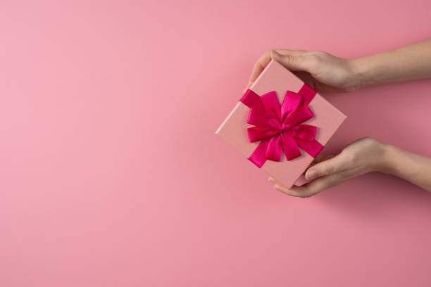 istock Valentine's Day celebration concept. A nice gift from a loved one. Box with a bow in female hands on a delicate pink background. Copy space. Flat lay. 1205156284