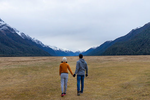 Young Asian couple holding hands walking into mountain Eglinton valley Fiordland National Park New Zealand