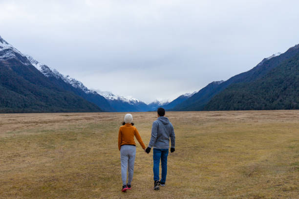 Photo of Young Asian couple holding hands walking into mountain Eglinton valley Fiordland National Park New Zealand