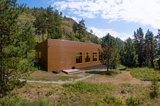 Modern house made from brown sandwich panel in the mountains and wood . The cottage is surrounded by trees. Sport gym building in natural place