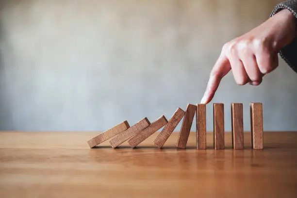 Closeup image of a finger try to stopping falling wooden dominoes blocks for business solution concept