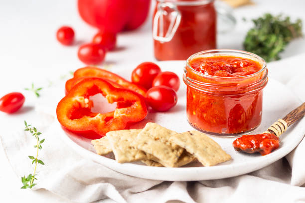 ajvar (mousse au poivre) ou tartinade de légumes rouges pindjur à base de paprika et tomates dans un bocal en verre sur table en pierre légère. nourriture indigène serbe. - chutney jar tomato preserved photos et images de collection