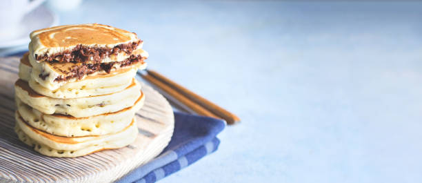 istock Stack of Stuffed chocolate nutella pancakes on wooden board on blue table background. American Breakfast Concept. Copy space. Banner for website 1205177662