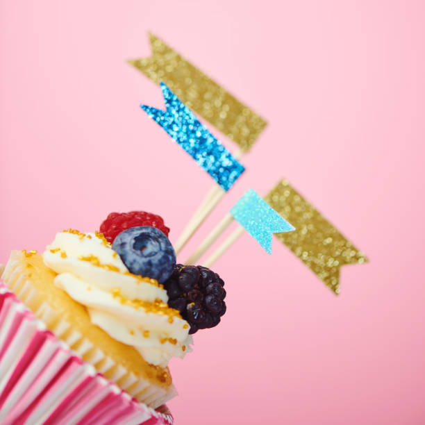 istock Celebration cupcake with flags and confetti on pink background 1205177723