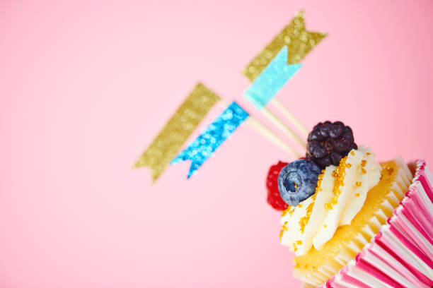 Celebration cupcake with flags and confetti on pink background