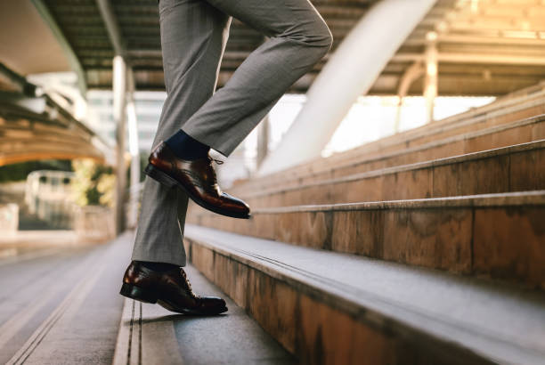 istock Motivation and challenging in Career Concept. Steps Forward into a Success. Low Section of Businessman Walking Up on Staircase. Modern Urban City as background 1205181196