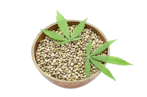 Cannabis Hemp seeds in a wooden bowl and green leaves isolated on white backgrounds