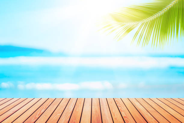 istock Blur tropical beach with bokeh sun light wave and palm tree on copy space empty old wood table abstract background. 1205194007