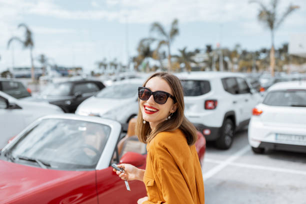 Happy woman with keys near the car at the parking Portrait of a beautiful young woman standing with keys near the red cabriolet at the car parking outdoors. Concept of a happy car buying or renting convertible photos stock pictures, royalty-free photos & images