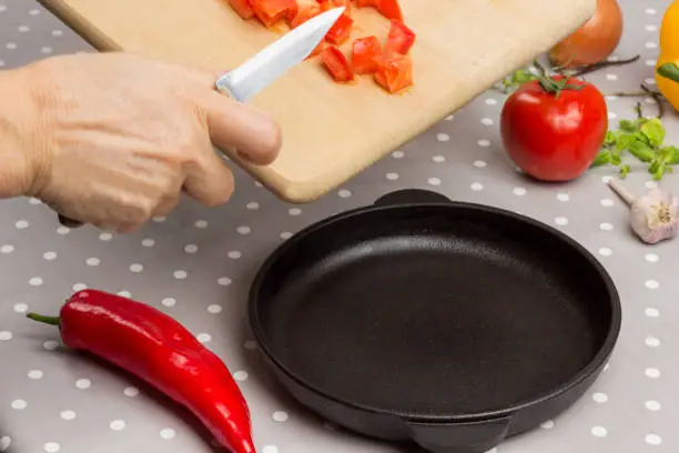 Photo of Hands put chopped tomatoes in an empty pan.