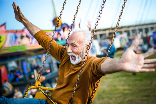 Happy mature man having fun on a chain swing ride at amusement park. Happy senior man shouting while riding on chain swing with his arms outstretched at amusement park. young at heart stock pictures, royalty-free photos & images