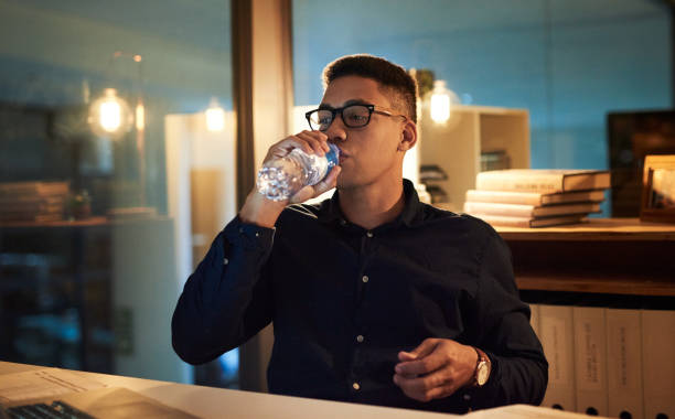 You could never quench his thirst for success Shot of a young businessman drinking bottled water during a late night at work quench your thirst pictures stock pictures, royalty-free photos & images