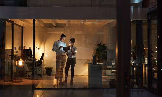 Shot of a young businessman and businesswoman using a digital tablet during a late night at work
