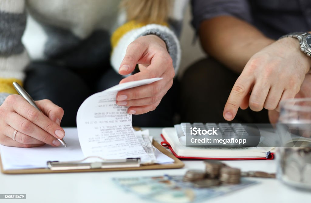 Month revenue of young couple Close-up view of man and woman making account of family income. Writing down and calculating expenses. Attentive review of finance. Calculator on desk. Economy concept Home Finances Stock Photo