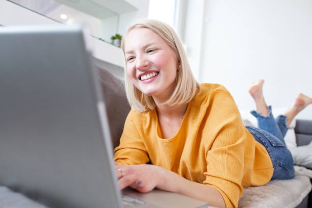 istock Smiling albino woman working from home, typing email on laptop, sitting on sofa. Surfing web at home. Side view of attractive young woman working on laptop and smiling while sitting on the couch 1205215139