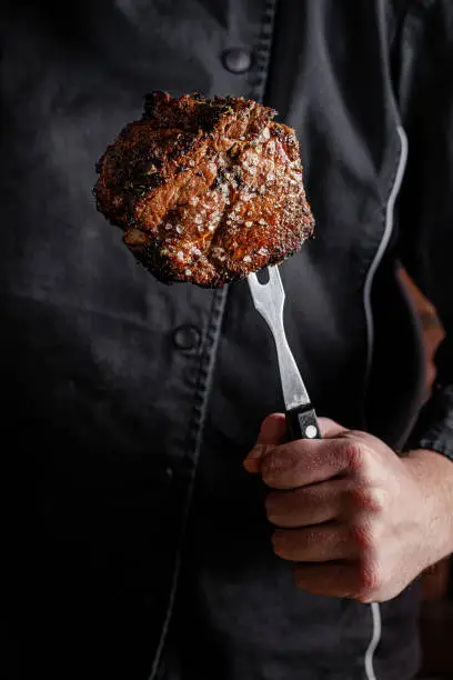 The chef cook is holding a beef steak in his hands on a fork. background image, copy space text