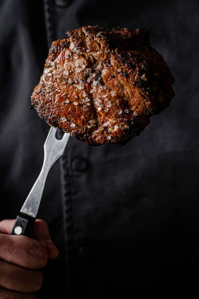 istock The chef cook is holding a beef steak in his hands on a fork. background image, copy space text 1205217049