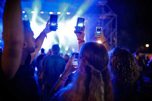 Unrecognizable fans taking picture of stage performers at music concert at night