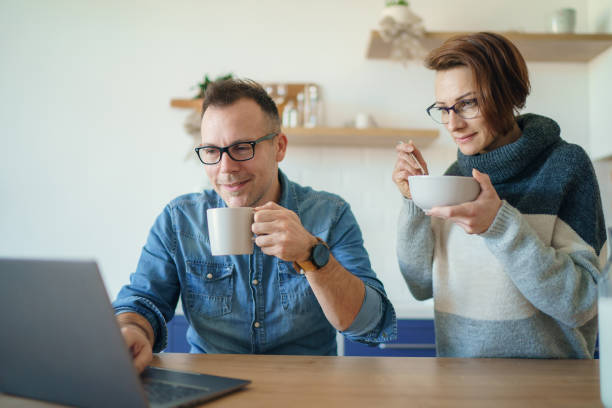 istock Beautiful young married couple having breakfast together working on laptop at table or reading news. Loving husband and wife making plans for vacation in the kitchen at home 1205222792
