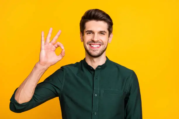 Portrait of confident cool smart freelancer promoter guy feel cheerful positive, expressions show ok sign select suggest ads wear casual style outfit isolated over yellow color background