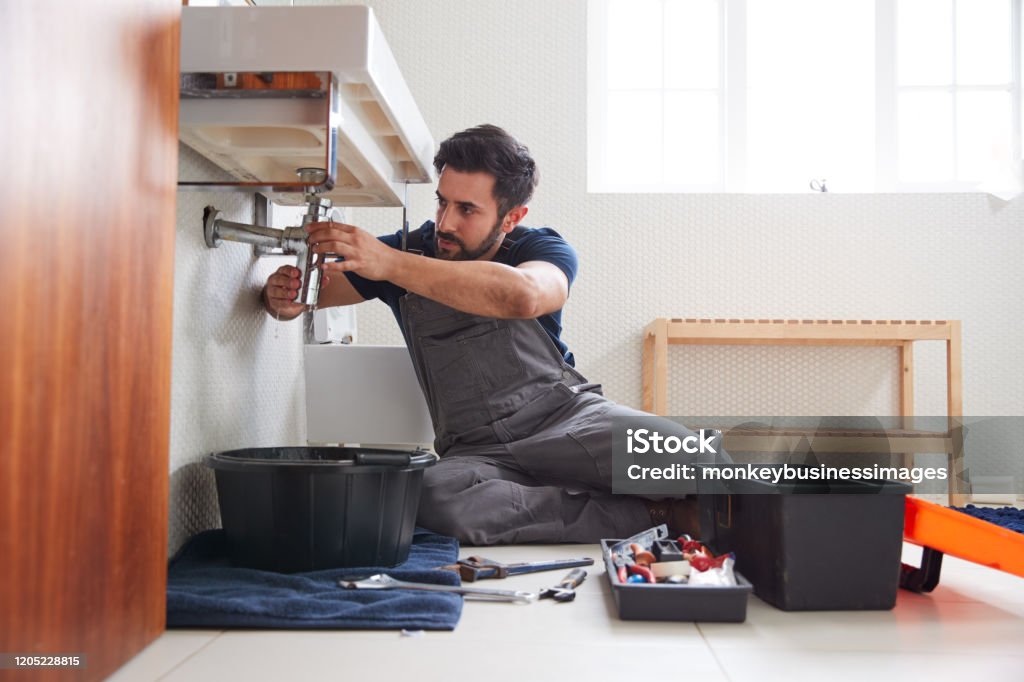 Plomero macho que trabaja para arreglar el fregadero con fugas en el baño casero - Foto de stock de Fontanero libre de derechos