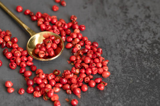 istock Pink pepper in a gold spoon on black large background. Copy space 1205229978