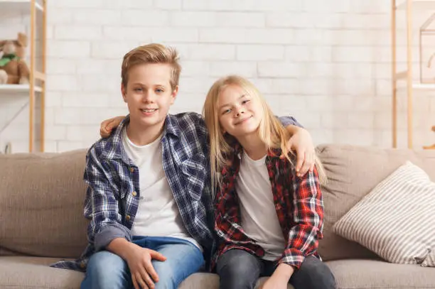 Photo of Brother And Sister Embracing Smiling Sitting On Couch At Home