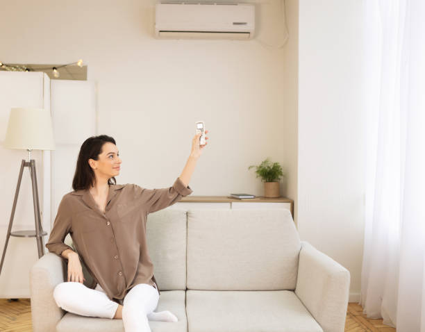istock Young woman switching on air conditioning sitting on sofa 1205232343