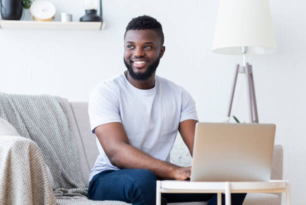 African male blogger using his laptop on couch at home