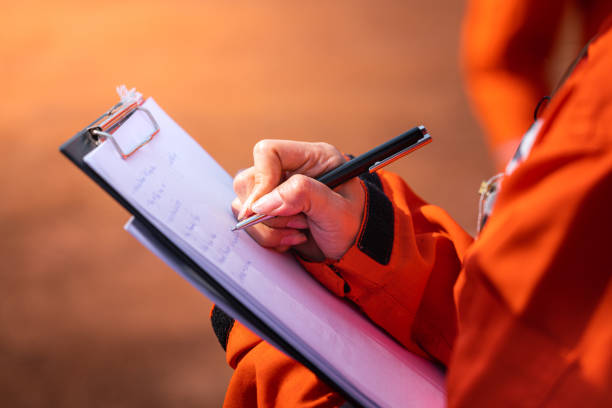 Writing note on paper - Audit and inspection in oil field operation. Safety officer/Supervisor is writing note on the checklist paper during perform audit and inspection in oil field operation. Close-up action and selective focus photo. unsafe workplace stock pictures, royalty-free photos & images