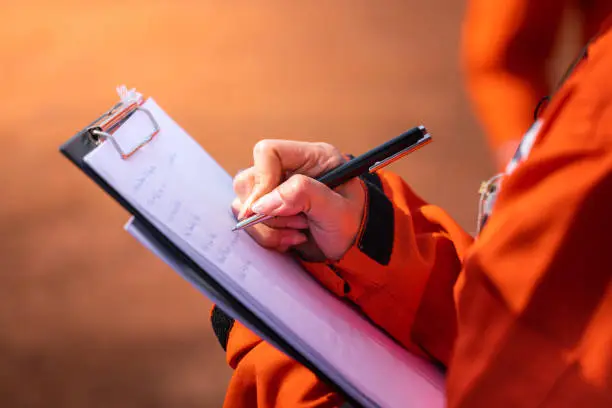 Safety officer/Supervisor is writing note on the checklist paper during perform audit and inspection in oil field operation. Close-up action and selective focus photo.