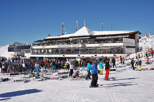 Ischgl, Austria - 7 February 2020: View of the busy Restaurant / cafe and lift station of Idalp in the Ischgl part of the Ischgl - Samnaun ski area which straddles Austria and Switzerland. Several diners are eating in the sunshine on the balcony areas.