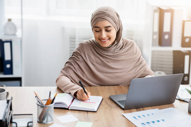 istock Smiling Islamic Businesswoman Using Laptop And Writing Notes, Managing Her Schedule 1205236474