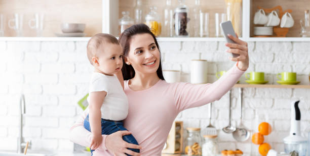 istock Happy mom taking photo with baby on smartphone at kitchen 1205237195