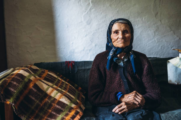 90-jährige frau sitzt auf dem bett - babushka stock-fotos und bilder