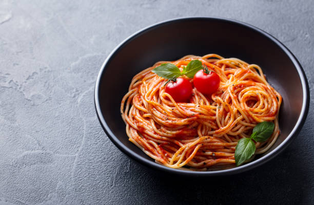 istock Pasta, spaghetti with tomato sauce in black bowl. Grey stone background. Close up. Copy space. 1205241568