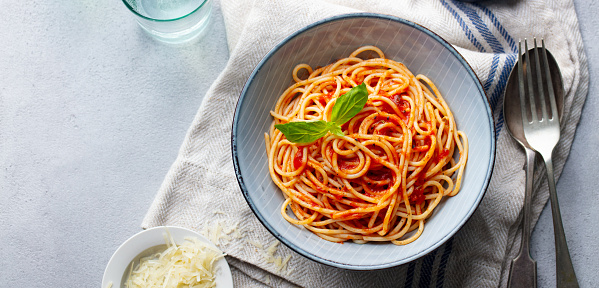 Pasta, spaghetti with tomato sauce and fresh basil in a bowl. Grey background. Top view. Copy space.