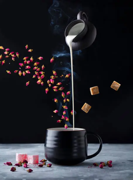 Photo of Rose flower tea with milk, flying ingredients. Black background.